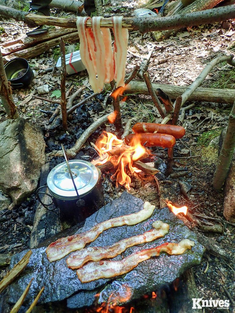 Here is a cook party with bacon hanging on a waugan (support) stick, sausages over a flame, water boiling, and the rock fryer in action.
