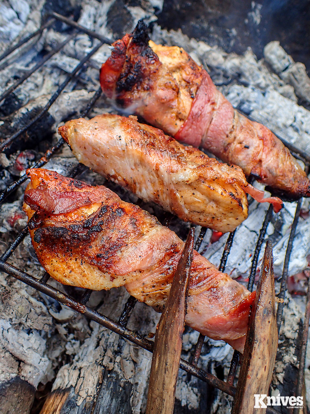 Coal cooking bacon-wrapped chicken breasts. A small grill can be placed directly on the coals for uniform cooking.