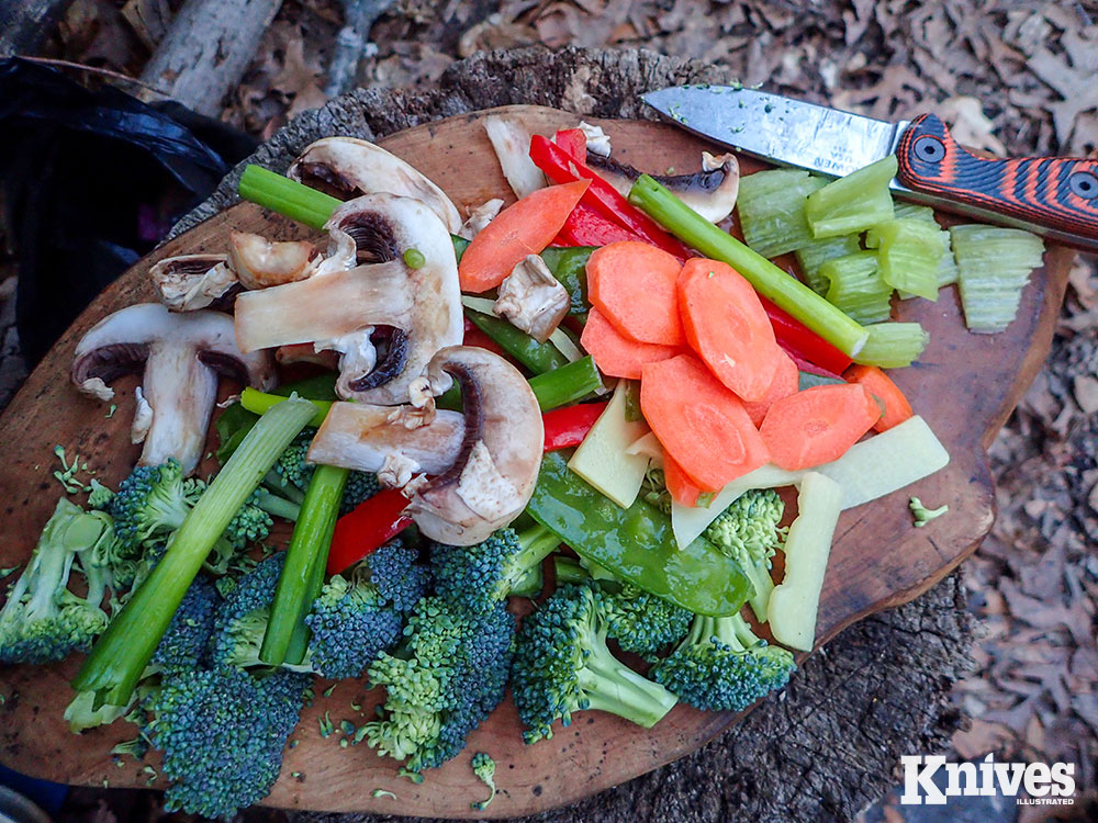 On a large cutting board, the author preps his stir fry while the fire burns, establishing coals to cook over. 
